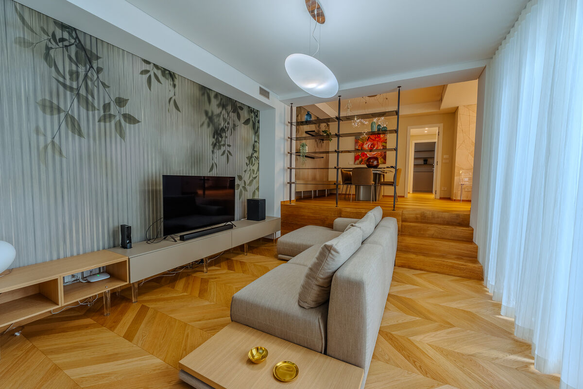 Soggiorno con divano modulare grigio, mobile TV e parete decorata a foglie