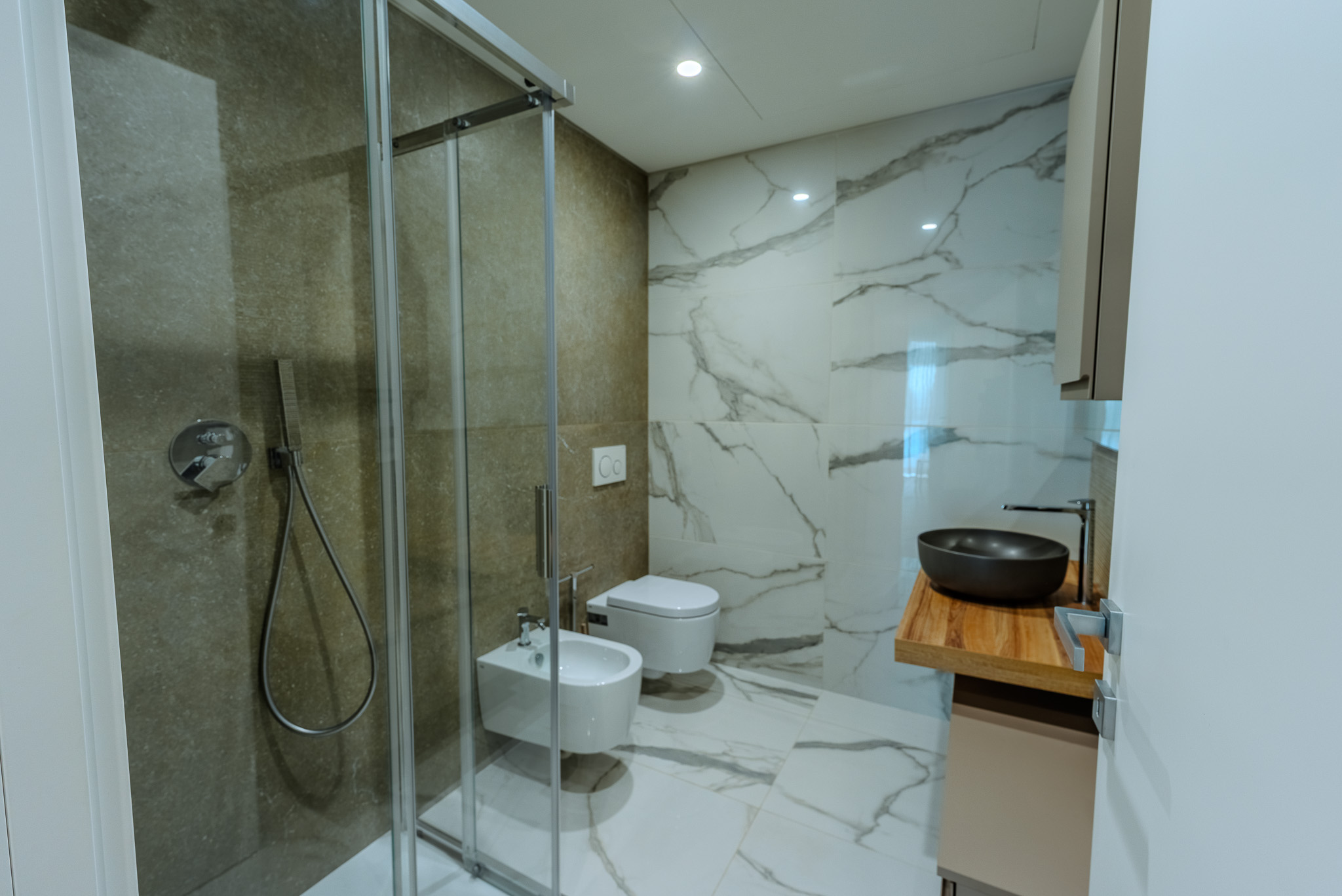 Bagno con doccia walk-in, wc, bidet e lavabo nero su top legno
