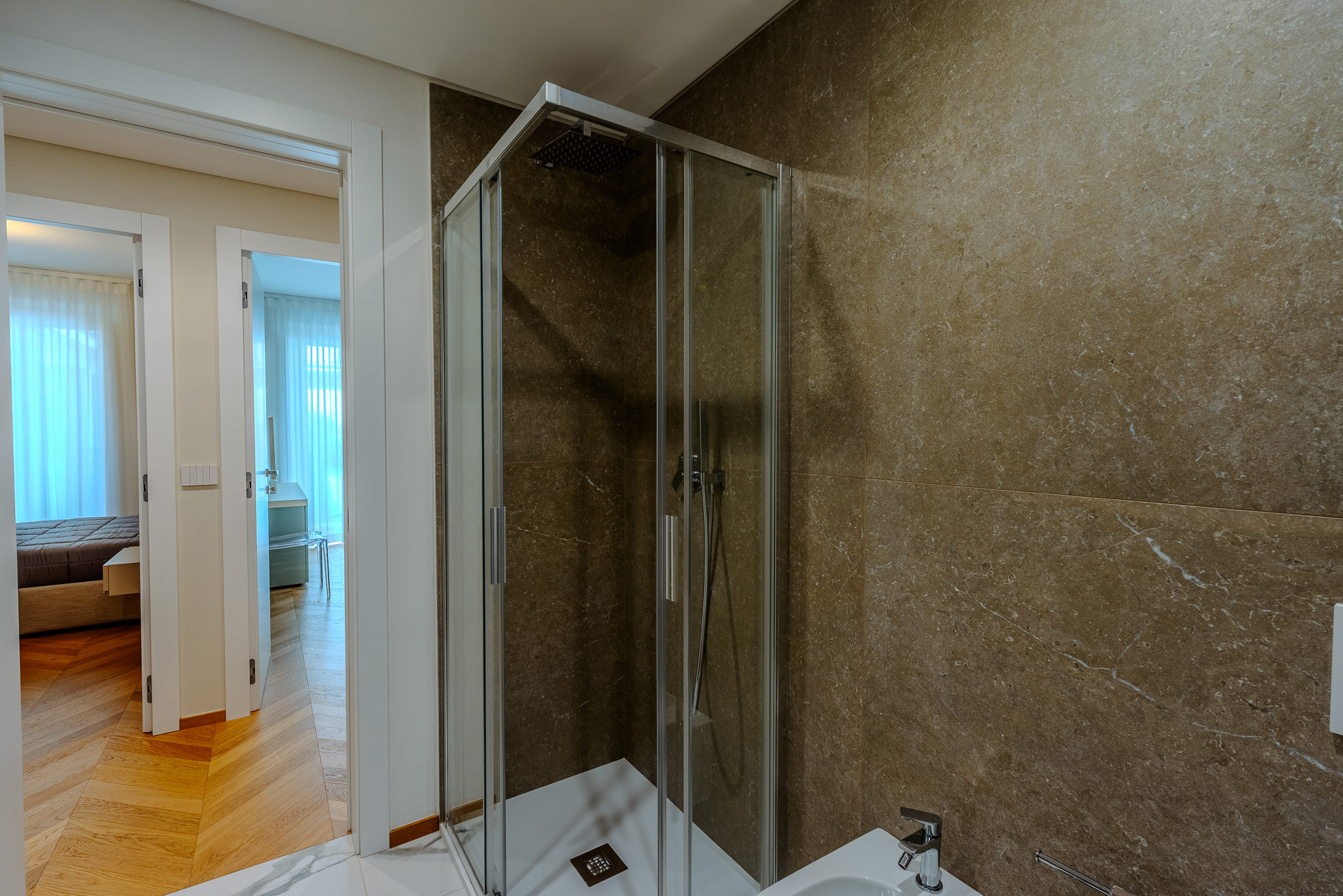 Bagno con doccia angolare in vetro e marmo travertino